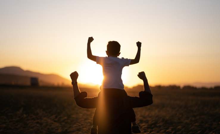 Kind auf den Schultern eines Erwachsenen bei Sonnenuntergang als Symbol für ein starkes Immunsystem